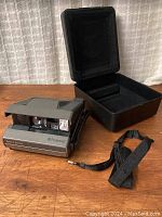 Polaroid Spectra System instant camera with carrying case and shoulder strap on wooden surface, case open showing foam interior