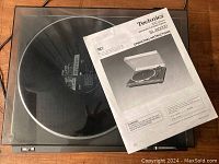 Top-down view of the Technics SL-BD20D turntable with vinyl on the platter and original manual on top, dustcover closed showing scratches and imperfections.