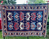 Full front view of rug hung on a fence showing central geometric medallion field and all borders
