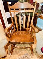Front view of solid wood rocking chair showing spindled back, turned vertical supports, and seat with visible wood grain and wear.