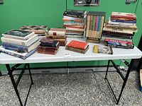 Wide view of the entire book collection displayed on a folding table showing multiple stacks and boxed sets.