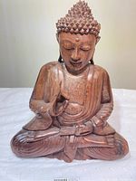 Front view of the carved wooden Buddha statue showing detailed facial features, hand gestures, and seated posture.