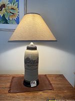Full view of the ceramic table lamp on wooden surface with lampshade illuminated