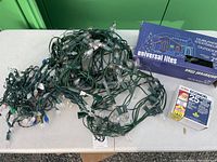 Two sets of outdoor Christmas lights on table. One set is Universal Lites with incandescent bulbs and green wiring in original box; the other set is Econolight LED lights in original package.