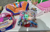 Overview of all doll items on table including clothing, furniture, and accessories