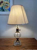 Full view of the vintage glass and brass lamp with cream fabric shade illuminated.