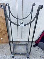 Black metal firewood stand shown empty against wooden backdrop.