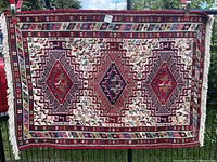 Full front view of the rug hanging on fence, showing overall pattern and fringe