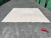 Full view of large light-colored Berber style carpet laid flat on gravel surface outdoors.