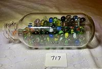 Glass milk jug filled with assorted marbles viewed from side angle on a white textured surface