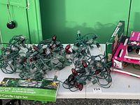 Photo showing multiple strands of Christmas lights on a white folding table against green wall background. Includes boxed sets and loose strands with various bulb types and colors.