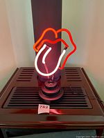 Front view of neon light sign shaped as iconic Rolling Stones lips and tongue logo lit up in red and white neon.