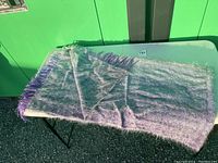 Wool throw blanket folded on a table showing mix of purple and gray colors with fringe edges.