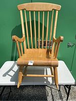 Front view of wooden rocking chair showing spindle back, armrests and seat with signed markings on front edge.