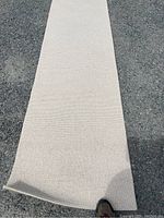 Full length image of beige Berber style runner carpet laid out on asphalt, showing entire carpet length and width with slight edge curl.