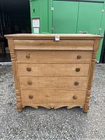 Front view showing five drawers with round knobs, turned front columns, scalloped skirt and natural wood finish