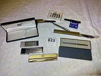 Overall lot display showing all pens, pen cases, and ink refills arranged on white patterned cloth