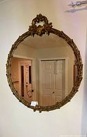 Front view of vintage ornate round mirror showing decorative carved gold-tone frame and reflection of interior.