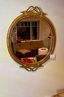 Wicker framed oval mirror reflecting a living room with couch and window, displayed on a light wall