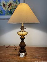 Front view of the lamp showing the wood base, amber glass reservoir, brass fitting, and beige fabric shade.