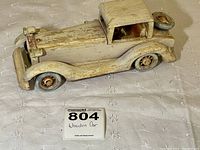 Side view of handmade vintage-style wooden car with white distressed paint, showing turned rubber tires and spare tire mounted on rear.