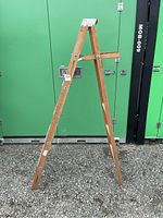 Full view of the closed wooden ladder showing metal hinge support and wood grain with patina.