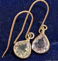 Close-up image showing two pear-shaped Zultanite earrings with gold hooks laid on a dark blue fabric.