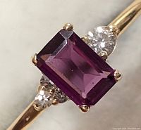 Close-up of rectangular deep red emerald-cut garnet center with flanking round diamonds