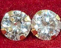 Close-up of two round clear cubic zirconia stones set in 14K gold four-prong settings displayed on a red background.