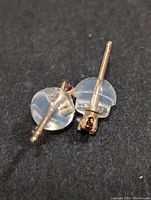 Close-up back view of two 14K gold stud earrings with clear plastic backs and posts visible