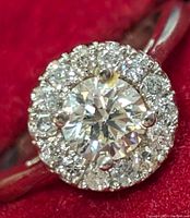 Front close-up of ring showcasing center stone and diamond halo on red background