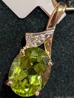 Close-up front angle of the gold pendant with oval green peridot and three small diamonds in setting