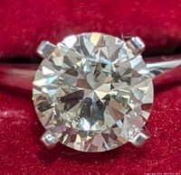 Close-up top view of round brilliant diamond in six-prong setting on white metal band against red velvet