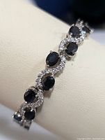 Close-up view of a sterling silver bracelet with oval blue sapphires and round clear cubic zirconia stones, displaying the design and stone setting.