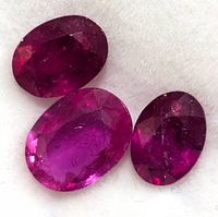 Close-up image of three oval faceted rubies in varying sizes with a deep red color on a light background.