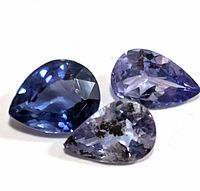Close-up image of three pear shaped tanzanite gemstones on white background showing color and cut details.