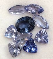 Top view of multiple tanzanite gemstones in various cuts and colors arranged on a white surface.