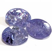 Three oval cut loose tanzanite gemstones displayed on a white background showing color and inclusions.