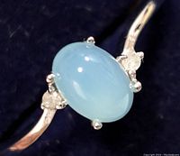 Close-up photo of oval light blue chalcedony stone in silver setting with two small diamonds on either side.