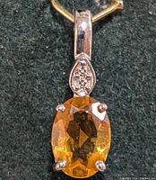 Close-up front view of silver pendant with faceted oval citrine and cluster of small stones above on green background.