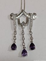 Front view of the silver necklace pendant showing clear cubic zirconia stones and three purple teardrop amethyst gemstones hanging down.
