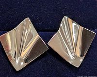 Front view of pair of silver geometric stud earrings on dark blue background showing folded design and shiny reflective surfaces.