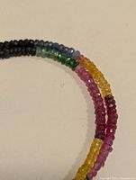 Closeup of faceted gemstone beads in multiple colors including blue, green, yellow, pink, and red hues in a strand of beads
