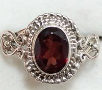 Close-up photo of silver ring with oval faceted garnet stone and detailed silverwork band.