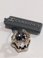Photo of silver pendant showing front and side views with attached Currency brand tag.
