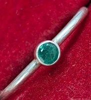 Close-up of silver ring with round green stone on red felt background.