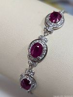 Close-up photo showing three oval ruby stones surrounded by cubic zirconia on sterling silver bracelet.