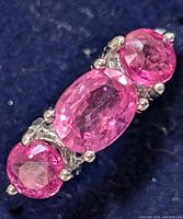 Close-up photo of silver ring with three pink faceted pink rubies, showing detail of stones and metal prongs