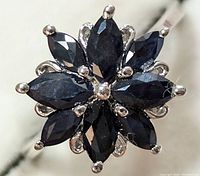 Close-up front view of silver ring with eight marquise-cut blue sapphire stones arranged like flower petals.