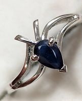 Close-up photo of the silver ring with the pear-shaped sapphire gemstone, showing the prong setting and open band design.